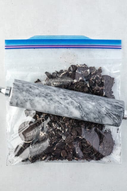 A marble rolling pin crushing Oreos in a gallon-sized Ziploc bag.