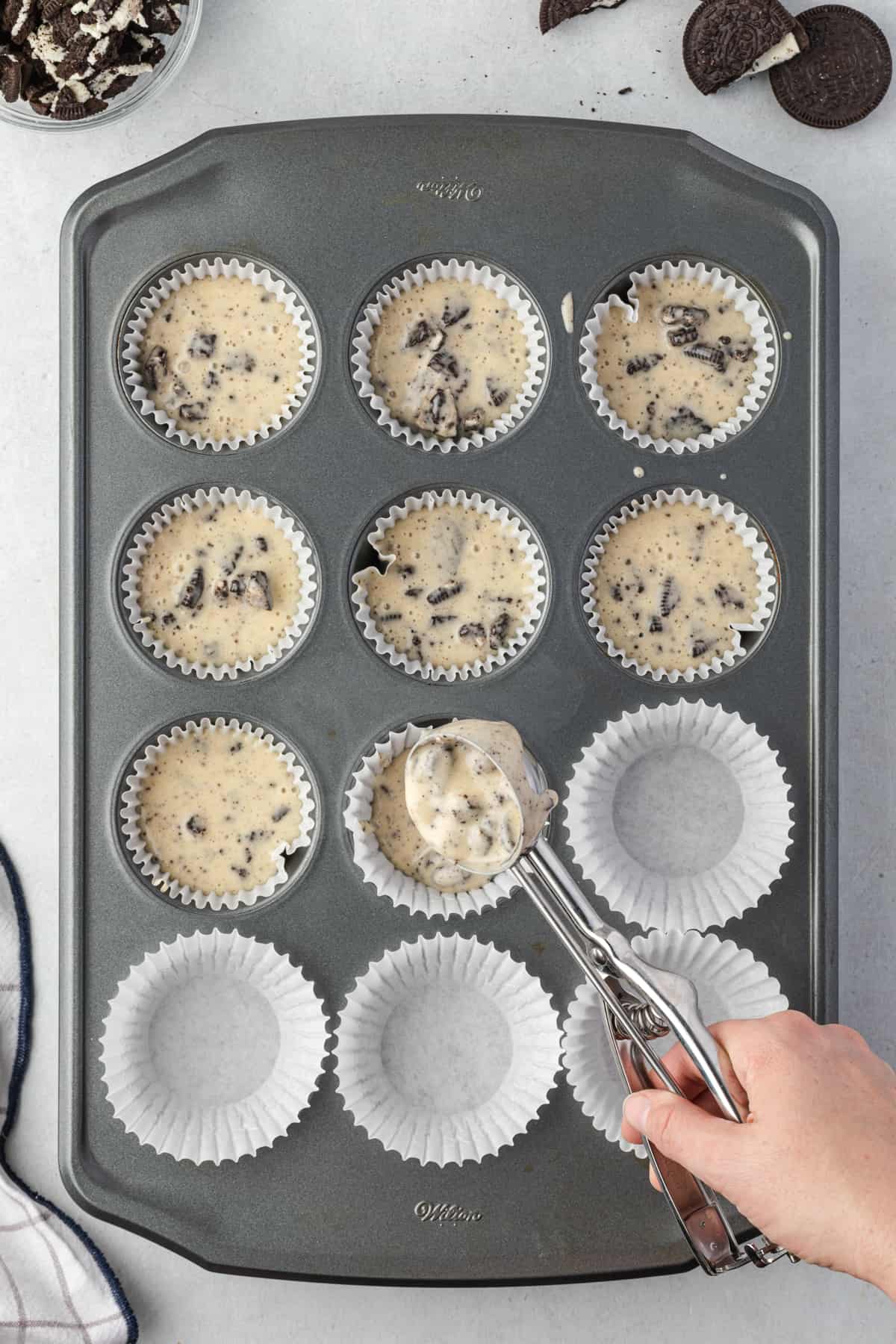 a large cookie scoop filling a pan with Oreo cupcake batter