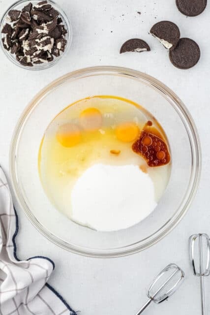 Ingredients for Oreo cupcakes in a glass mixing bowl, eggs, vanilla, oil and sugar