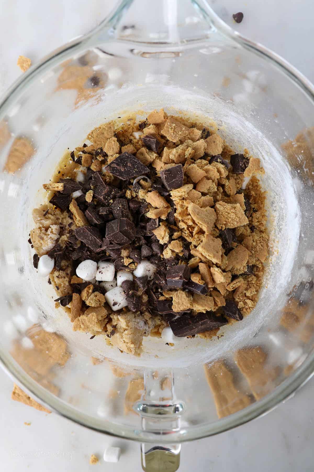 Chocolate, graham crackers, and marshmallows addd to cookie dough in a bowl.