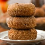 Three apple cider donuts stacked on top of one another on a white plate.