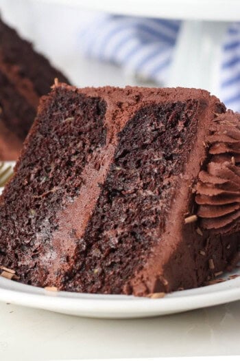 A slice of frosted chocolate zucchini cake laying on a plate.