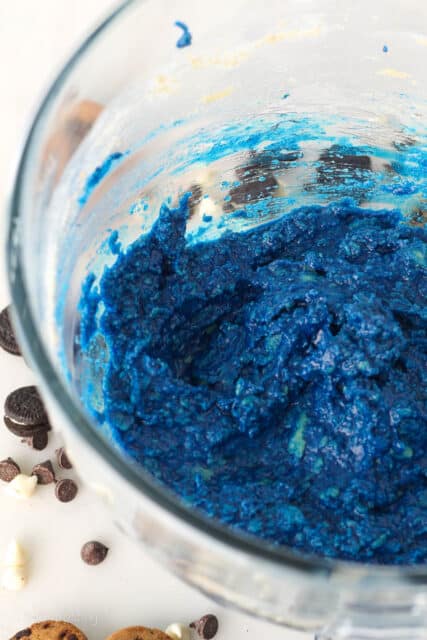 Blue-colored cookie dough in a glass mixing bowl.
