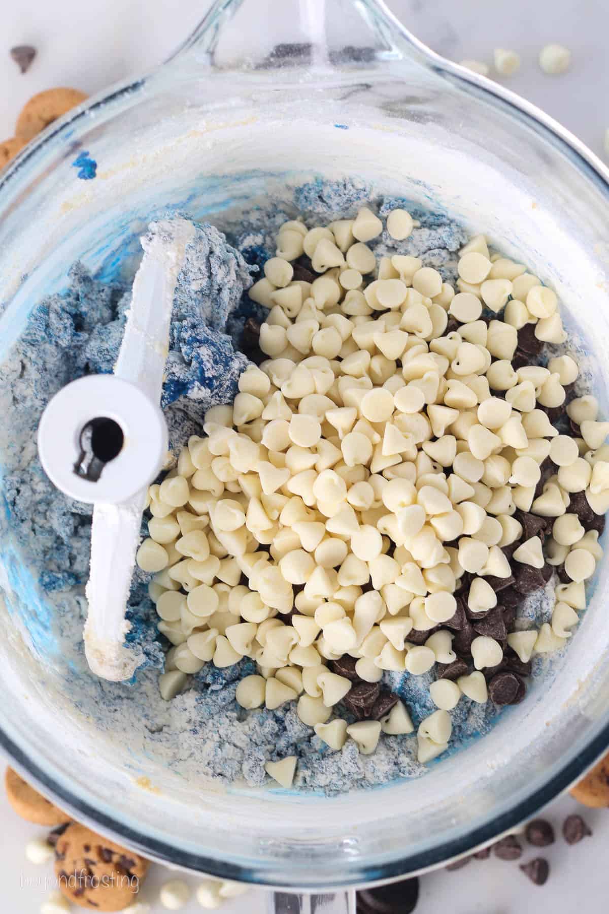 White chocolate chips and chocolate chips added to a bowl of blue cookie dough.