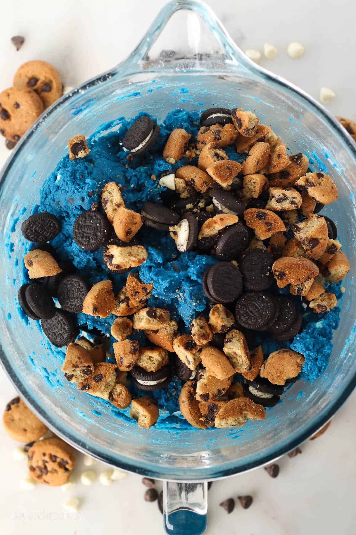 Chopped Oreos and Chips Ahoy cookies added to a bowl of blue Cookie Monster cookie dough.