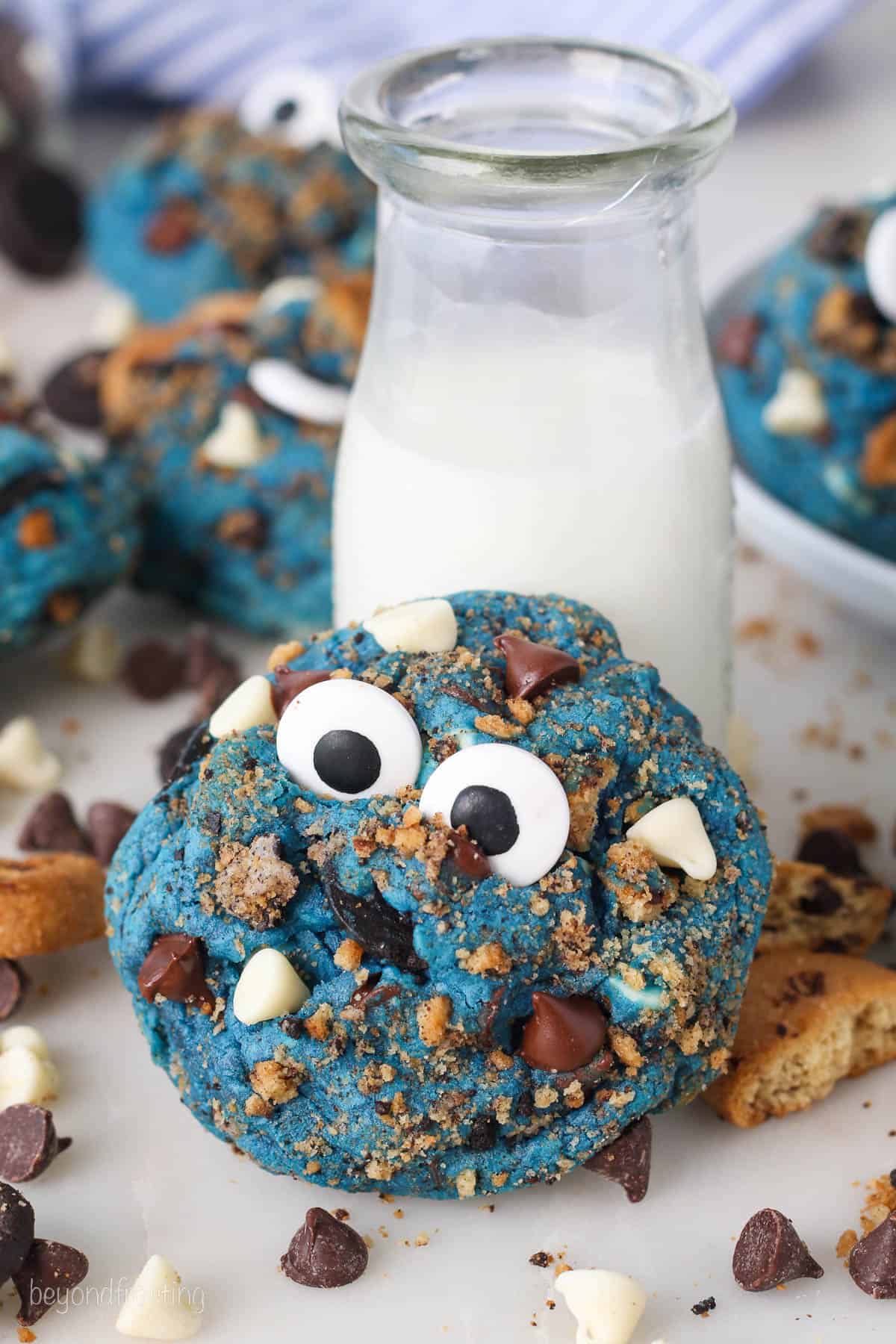 A Cookie Monster cookie leaning against a jar of milk, with more cookies in the background.