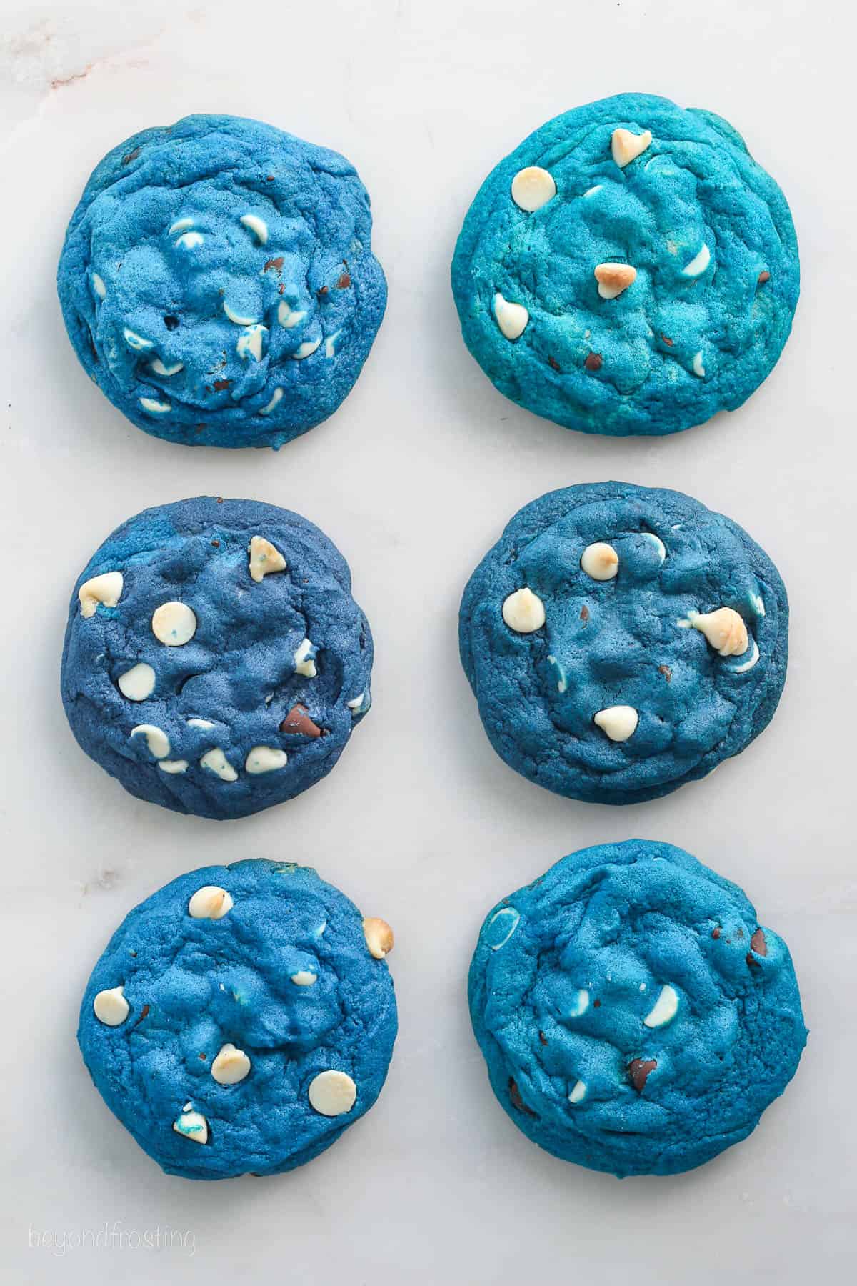 Six chocolate chip cookies dyed various shades of blue using gel food coloring.