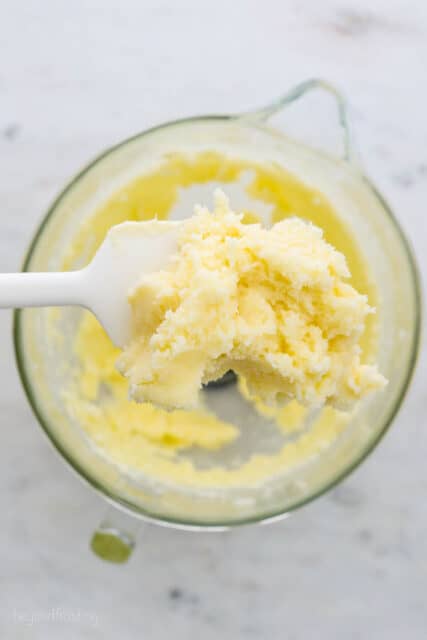 Overhead view of a spatula holding up a scoop of butter creamed together with sugar over a mixing bowl.