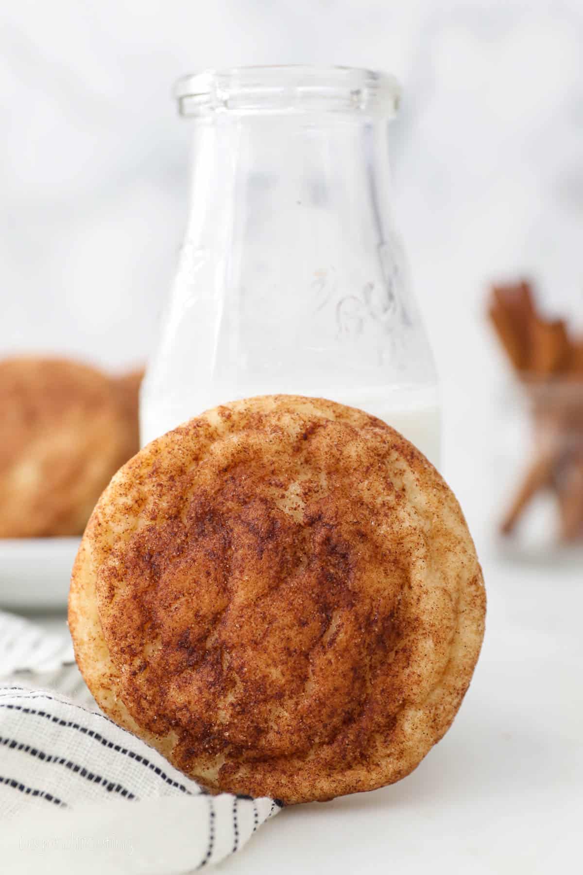 Close up of a snickerdoodle cookie propped up against a jug of milk on a white countertop.