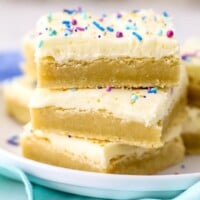 Three frosted sugar cookie bars stacked on top of one another on a plate.