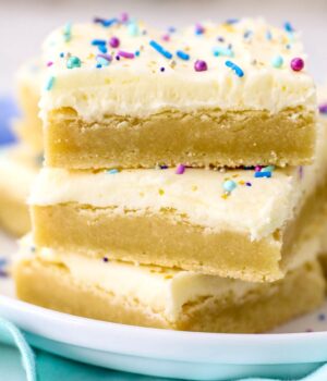 Three frosted sugar cookie bars stacked on top of one another on a plate.