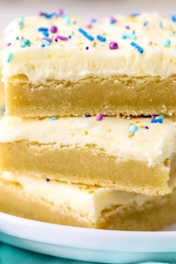 Three frosted sugar cookie bars stacked on top of one another on a plate.