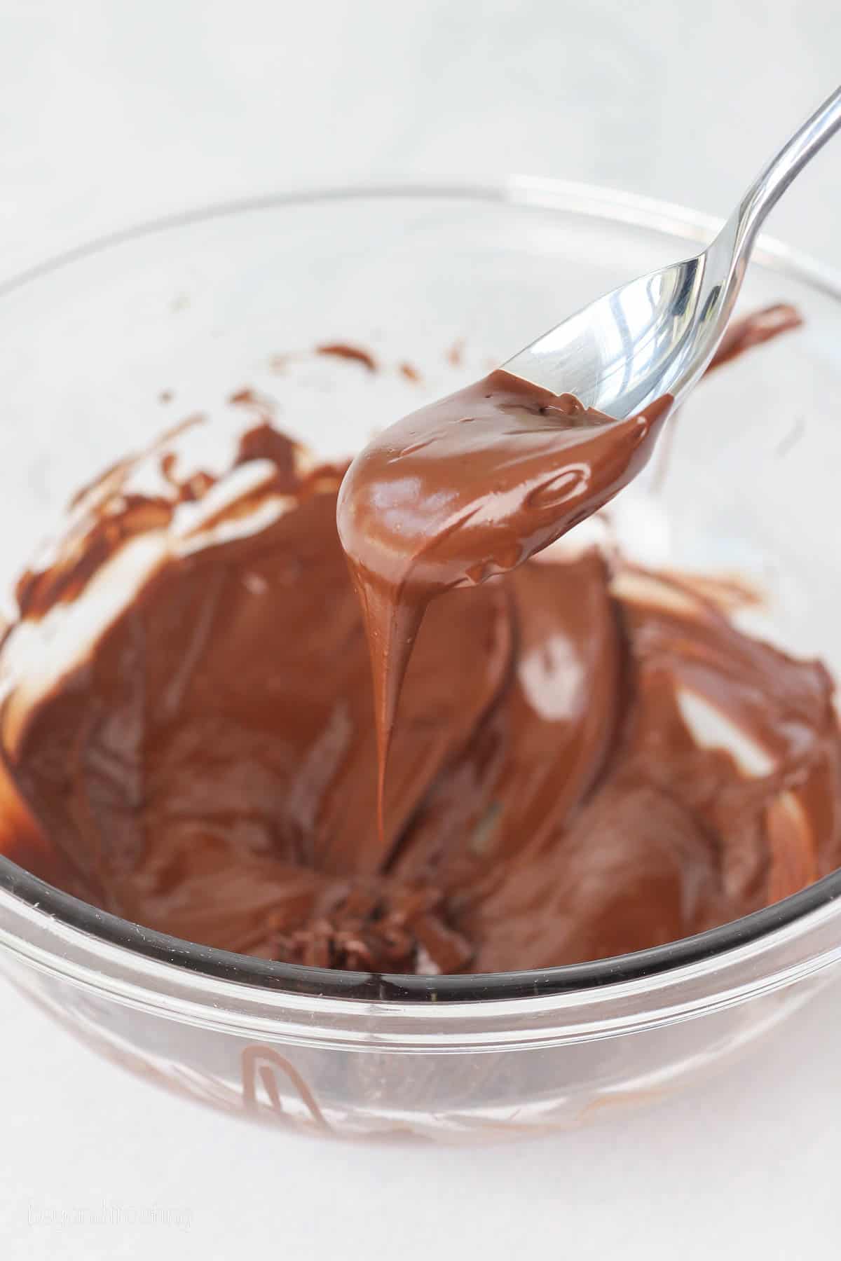 A spoon dipped into a bowl of melted chocolate chips.