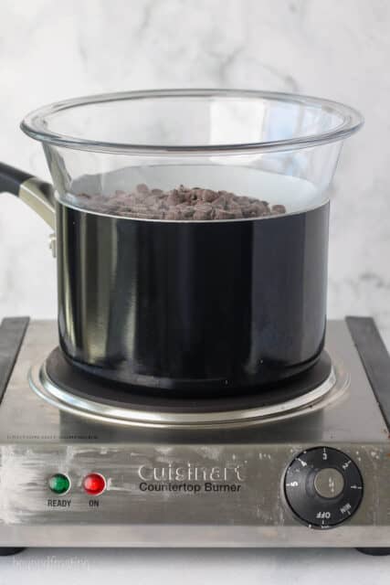 Side view of a double boiler set up on a stovetop, with the top bowl filled with chocolate chips.