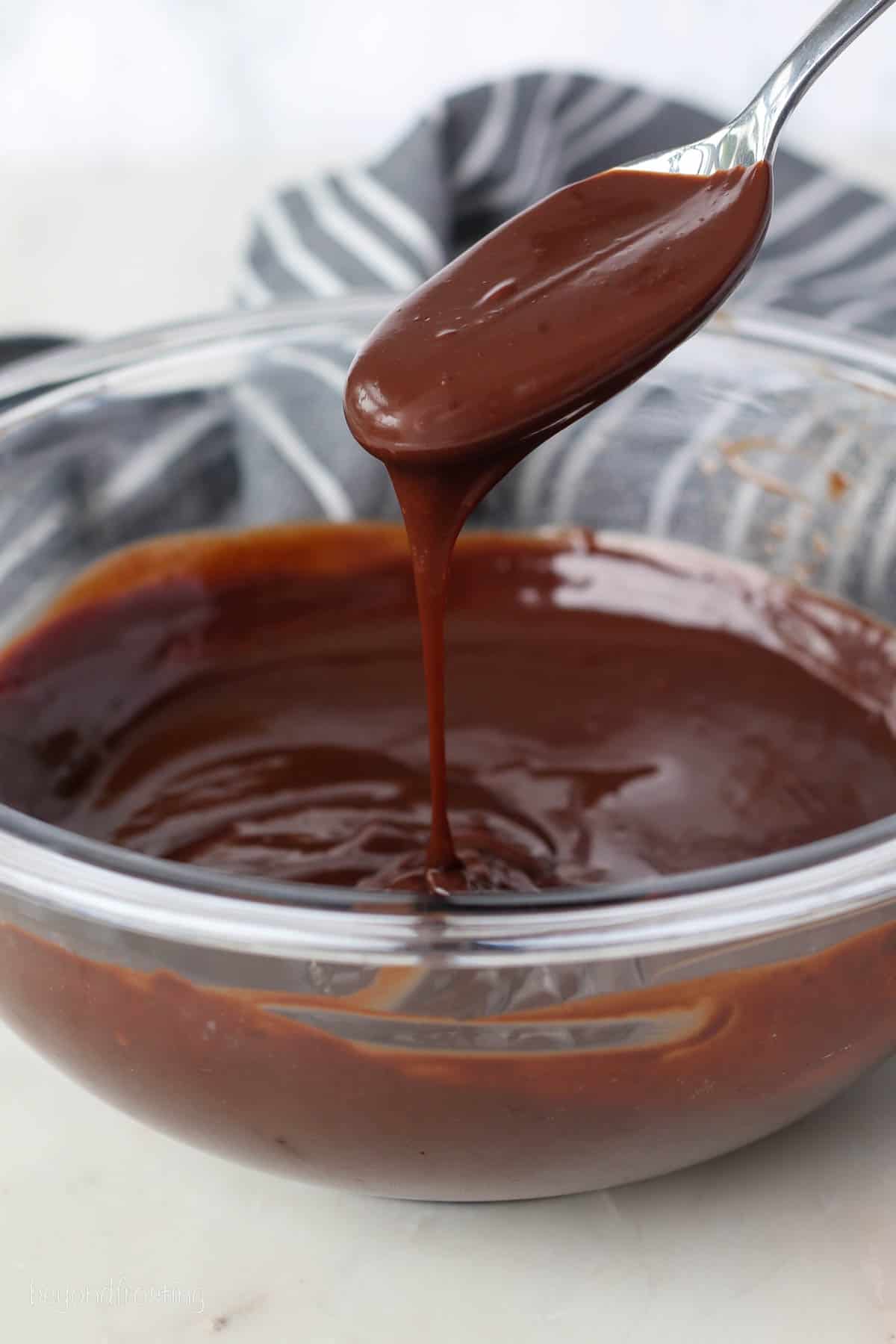 Chocolate ganache dripping from a spoon into a glass bowl.