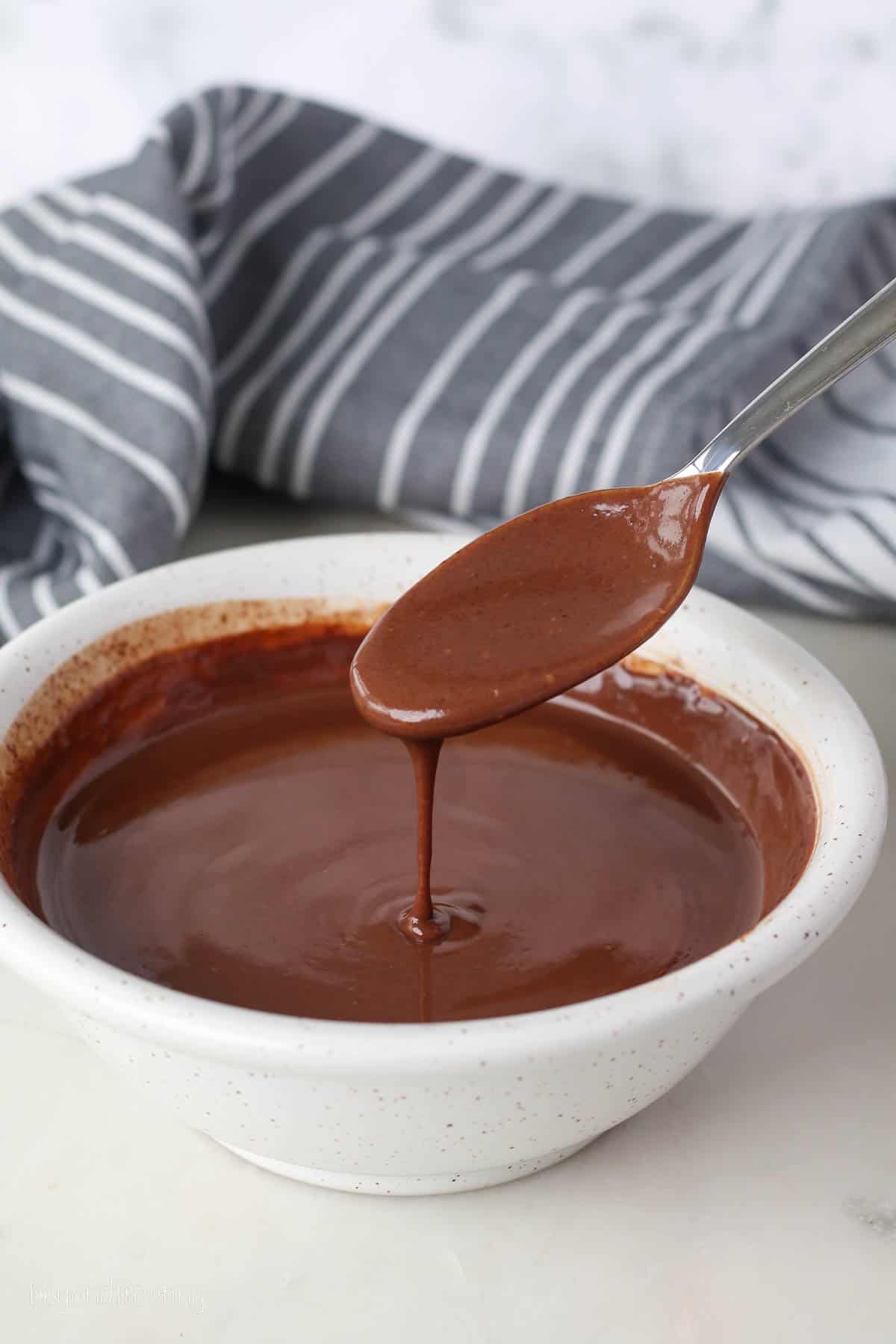 Chocolate ganache dripping from a spoon into a small white bowl.