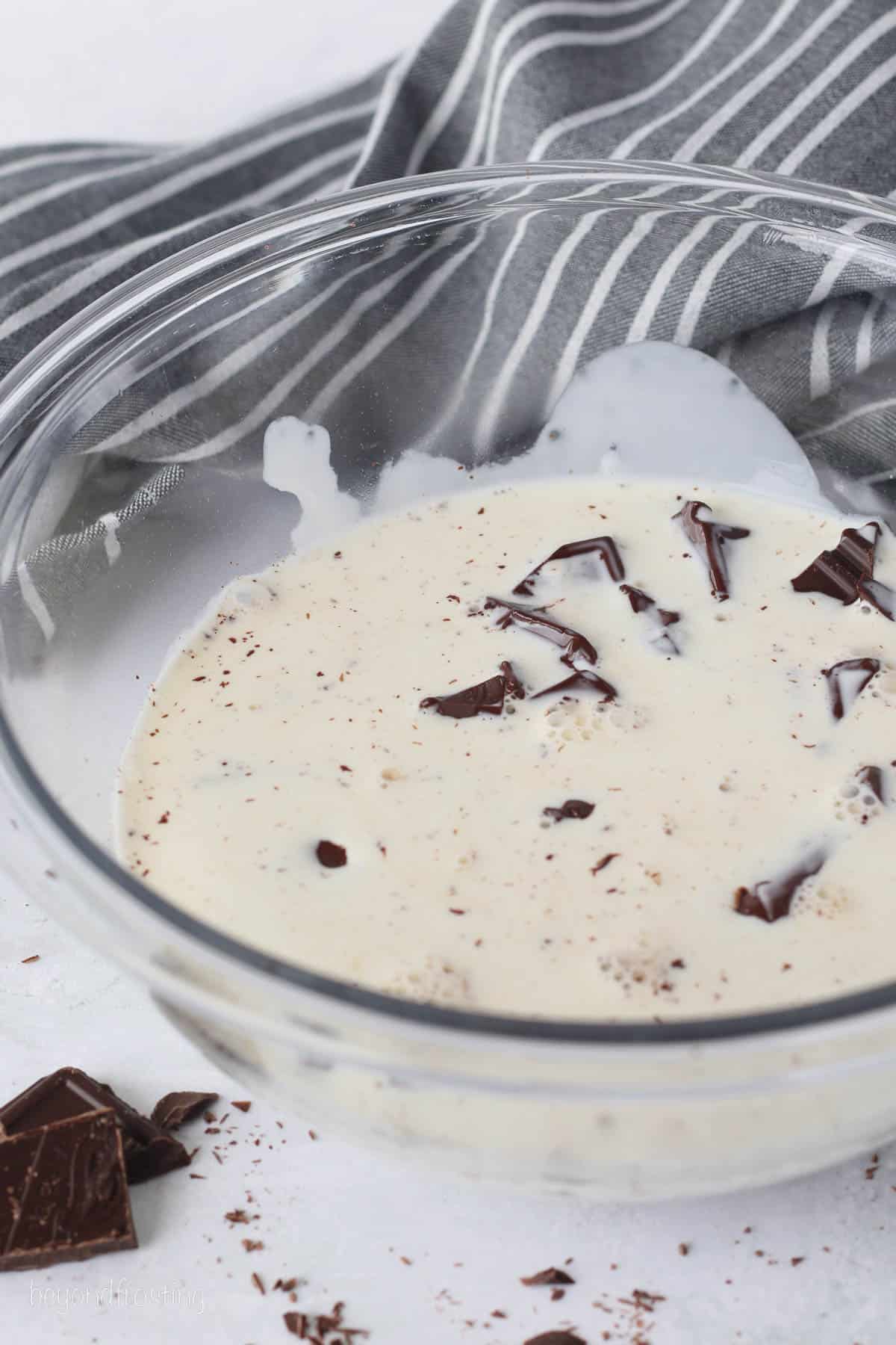 Heated heavy cream combined with chopped chocolate in a glass bowl.
