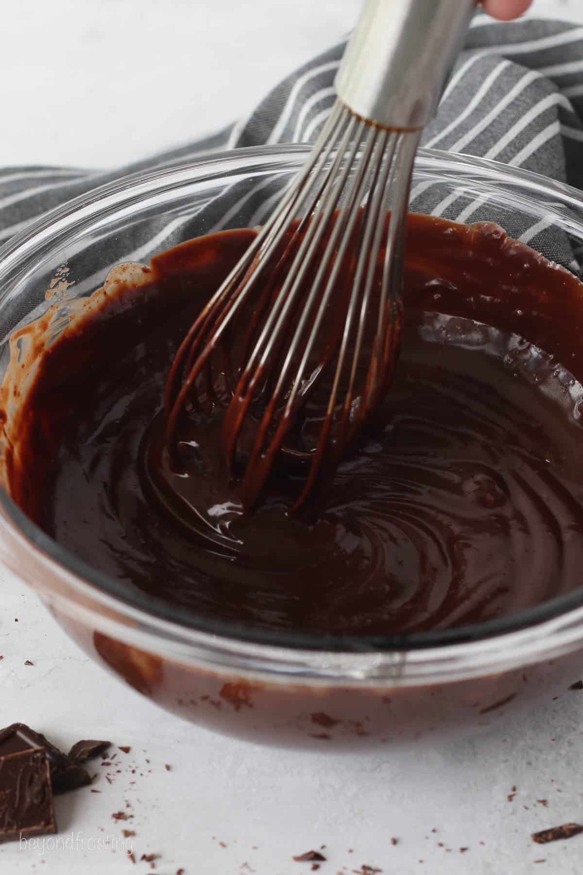 Chocolate and cream whisked together in a glass bowl to make chocolate ganache.
