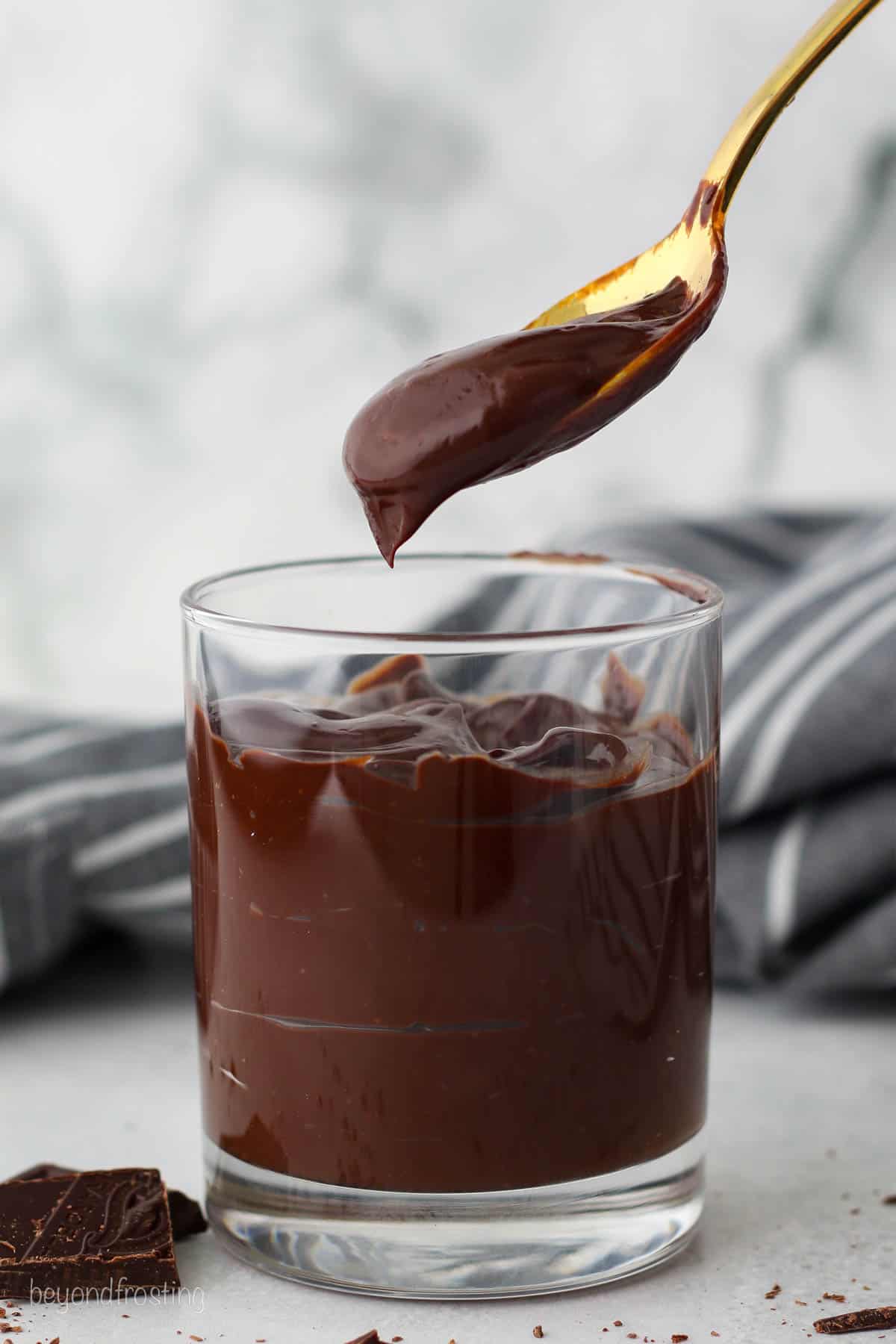 A spoonful held over a glass tumbler filled with chocolate ganache.