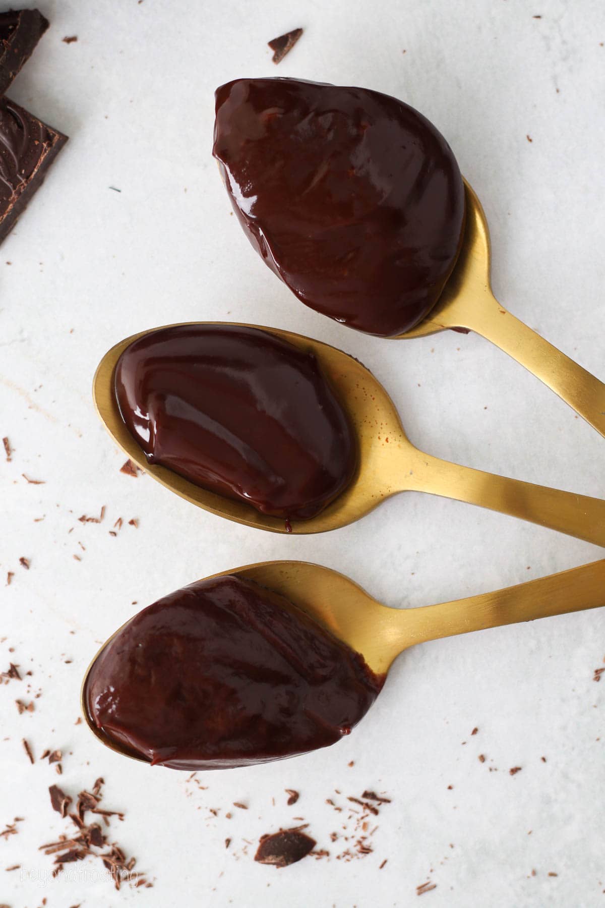Overhead view of three spoonfuls of chocolate ganache on a white countertop.