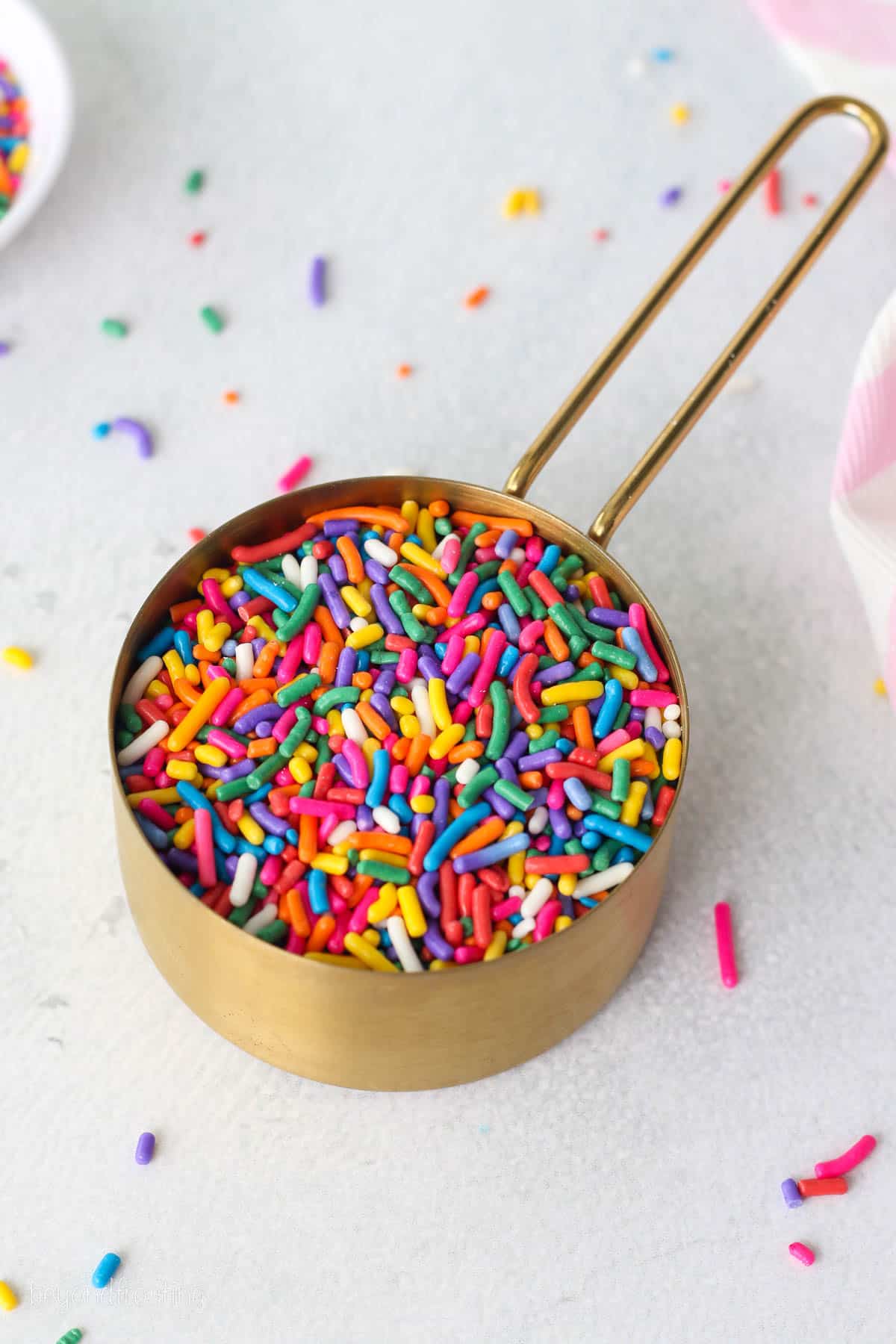 A measuring cup filled with rainbow sprinkles on a countertop.