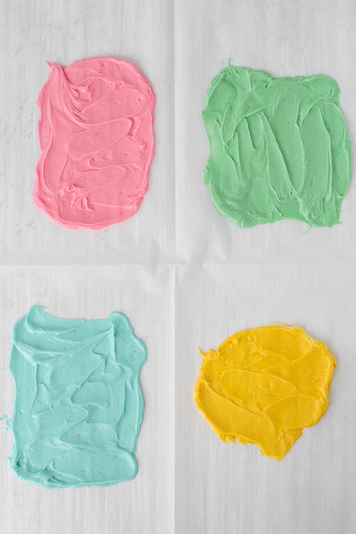 Pink, green, blue, and yellow melted chocolate spread into thin layers on a piece of parchment paper.