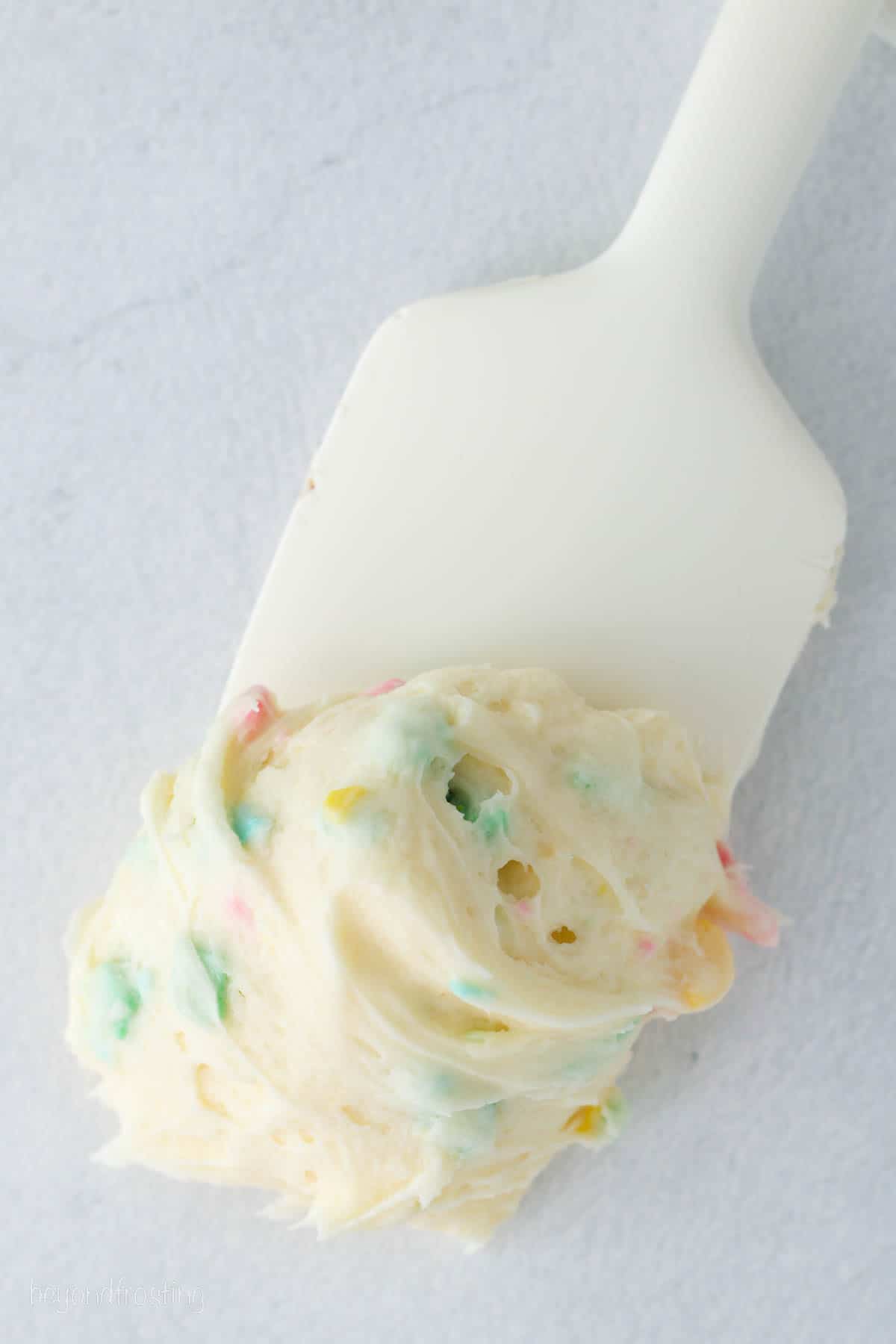 A scoop of confetti frosting at the end of a white spatula.
