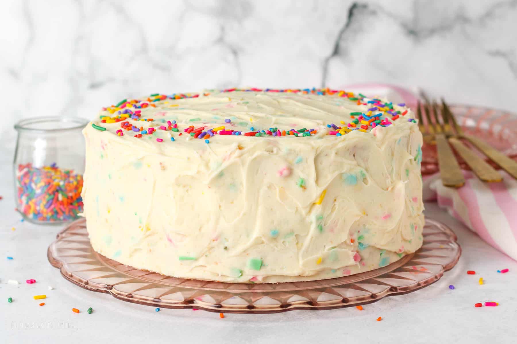 A whole frosted confetti cake decorated with sprinkles on a plate.