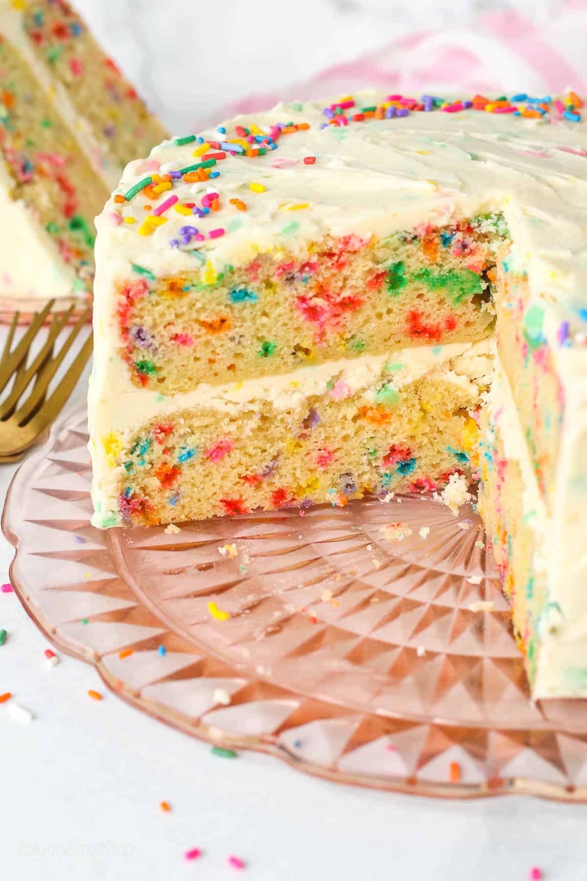 A frosted confetti cake on a plate with slices missing.