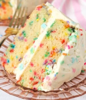A slice of confetti cake frosted with confetti frosting on a plate.