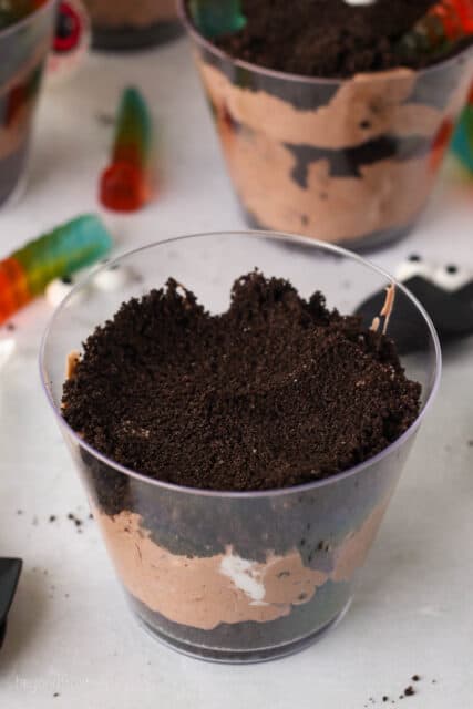 A partially assembled Halloween dirt cup with layers of Oreo mousse and Oreo crumbs.