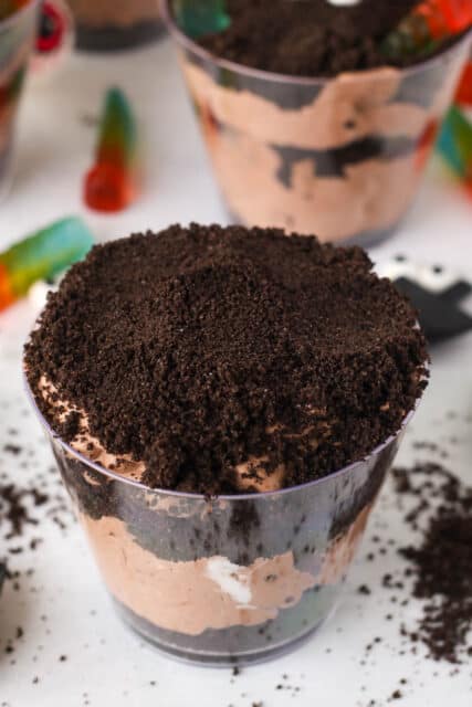 The final layer of Oreo crumbs is added to an assembled Halloween dirt cup.