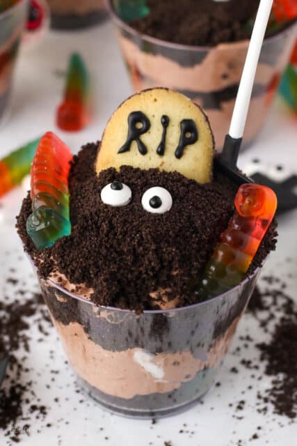An assembled Halloween dirt cup decorated with a Milano cookie headstone, candy eyes, and gummy worms.