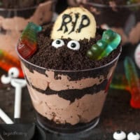 Close up of a Halloween dirt cup decorated with a Milano cookie headstone, candy eyes, and gummy worms.