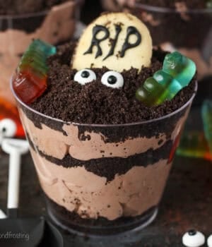 Close up of a Halloween dirt cup decorated with a Milano cookie headstone, candy eyes, and gummy worms.