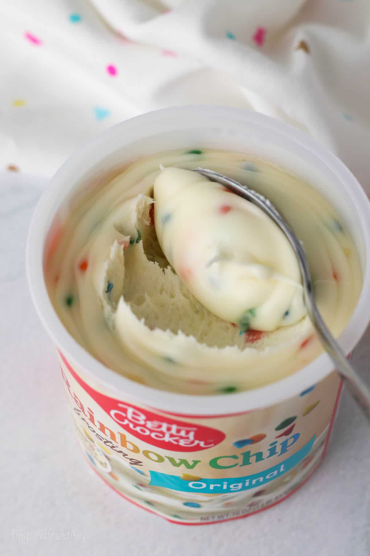 A container of Betty Crocker Rainbow Chip Frosting with a spoon.