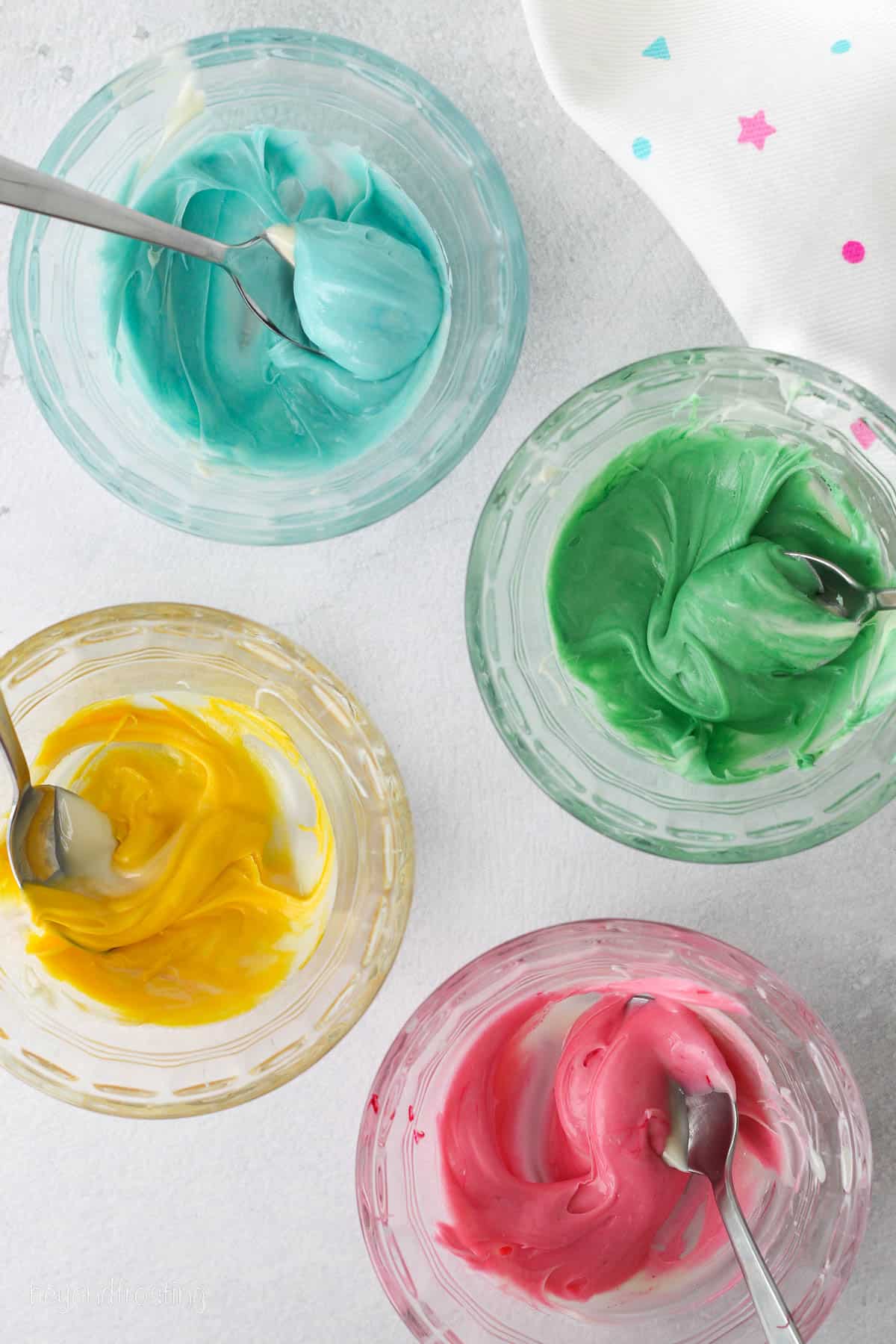 Overhead view of bowls of blue, green, pink, and yellow melted chocolate.