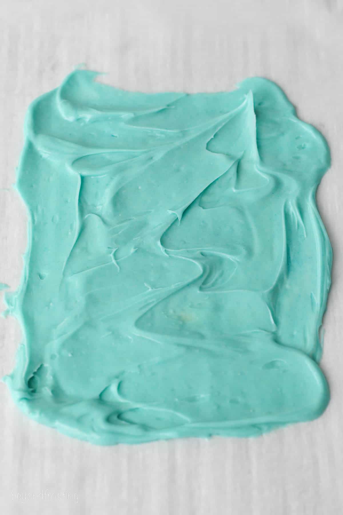 Blue melted chocolate spread in a thin layer on a piece of parchment paper.