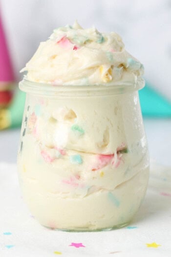 Rainbow chip frosting in a glass jar on a countertop.