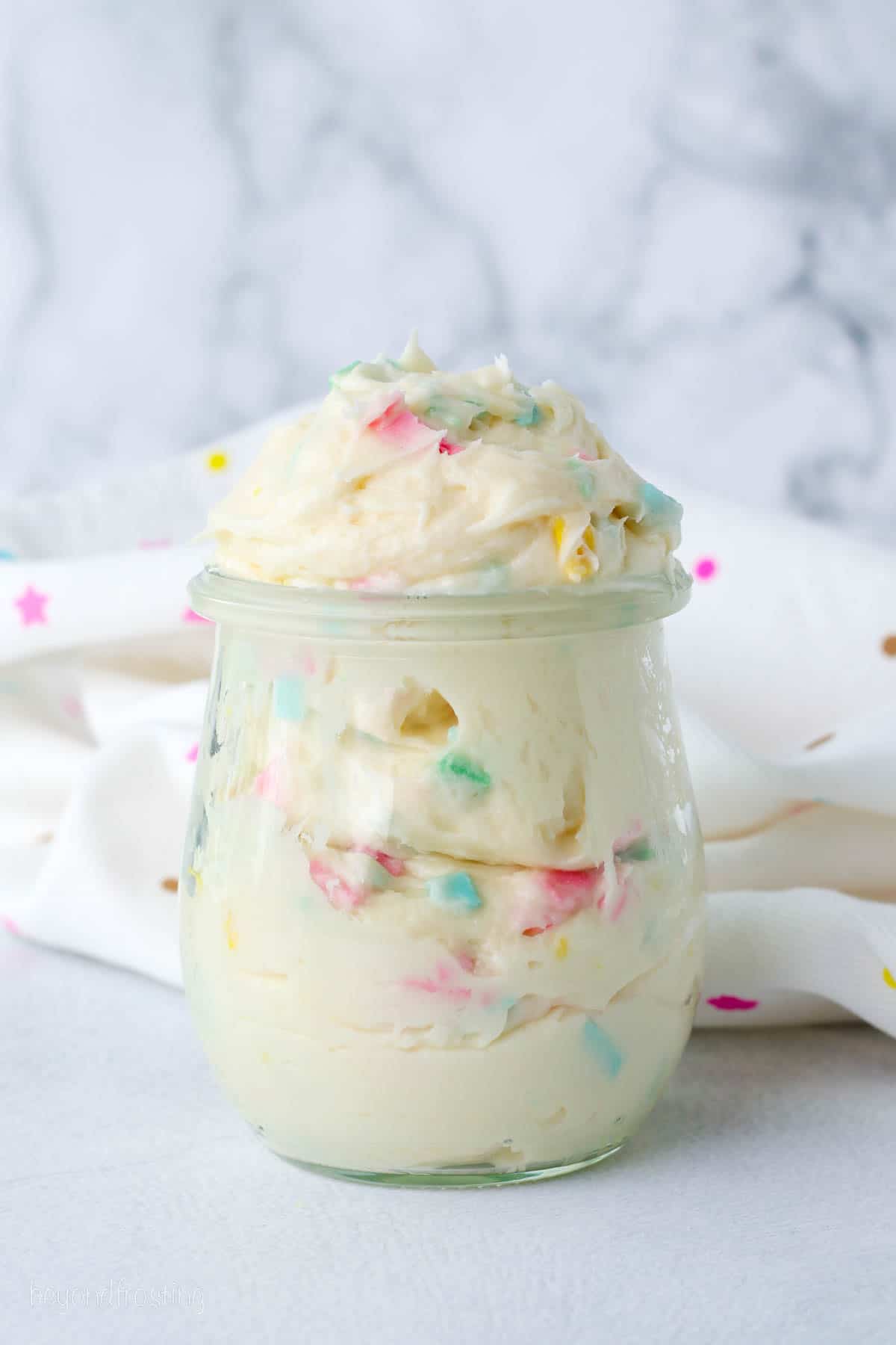 Rainbow chip frosting in a glass jar on a countertop.