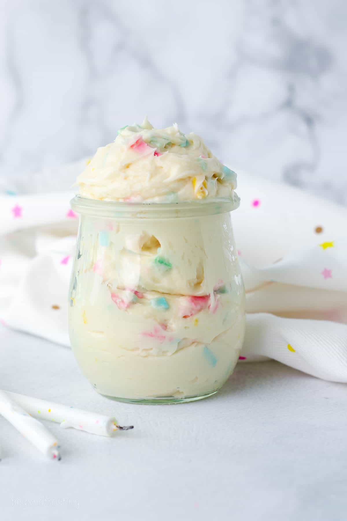 Rainbow chip frosting in a glass jar on a countertop.