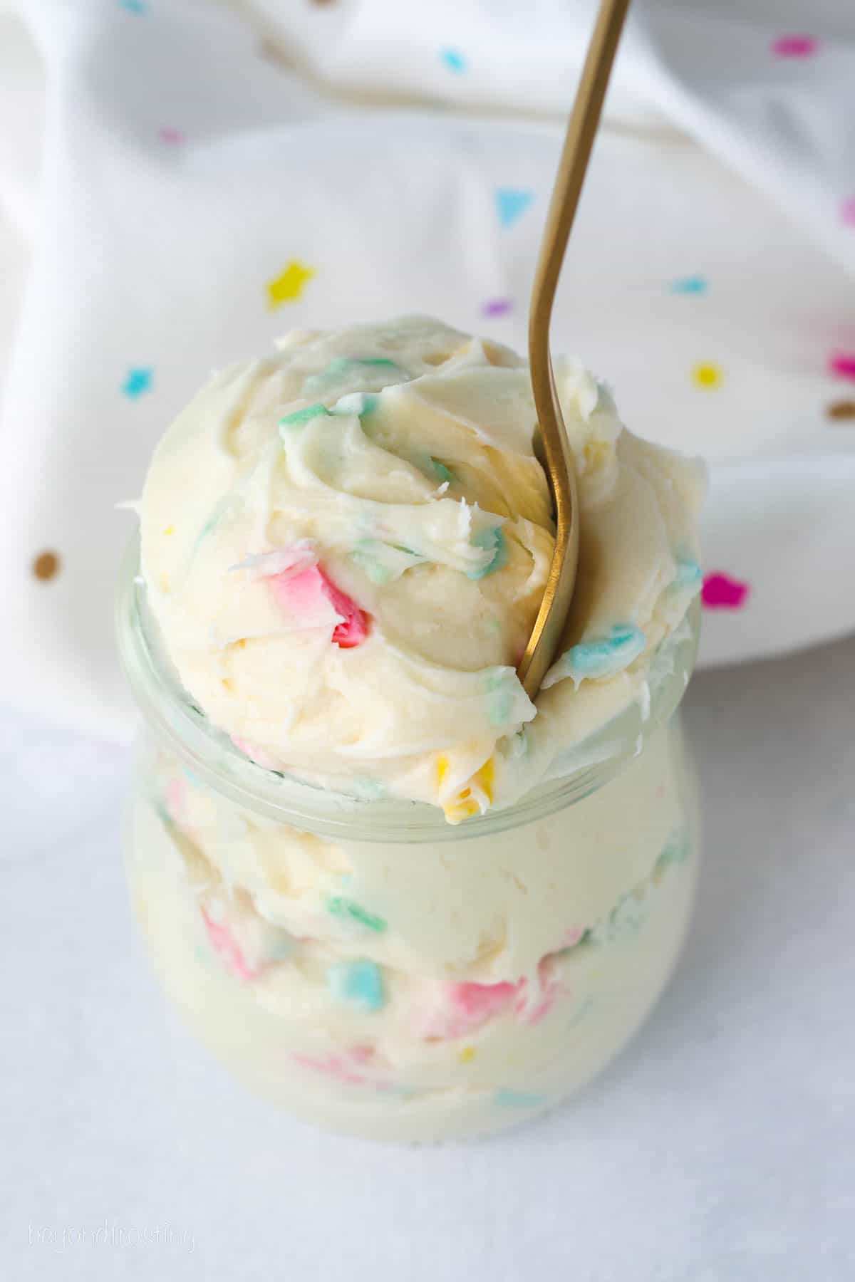 Confetti frosting in a glass jar with a spoon.
