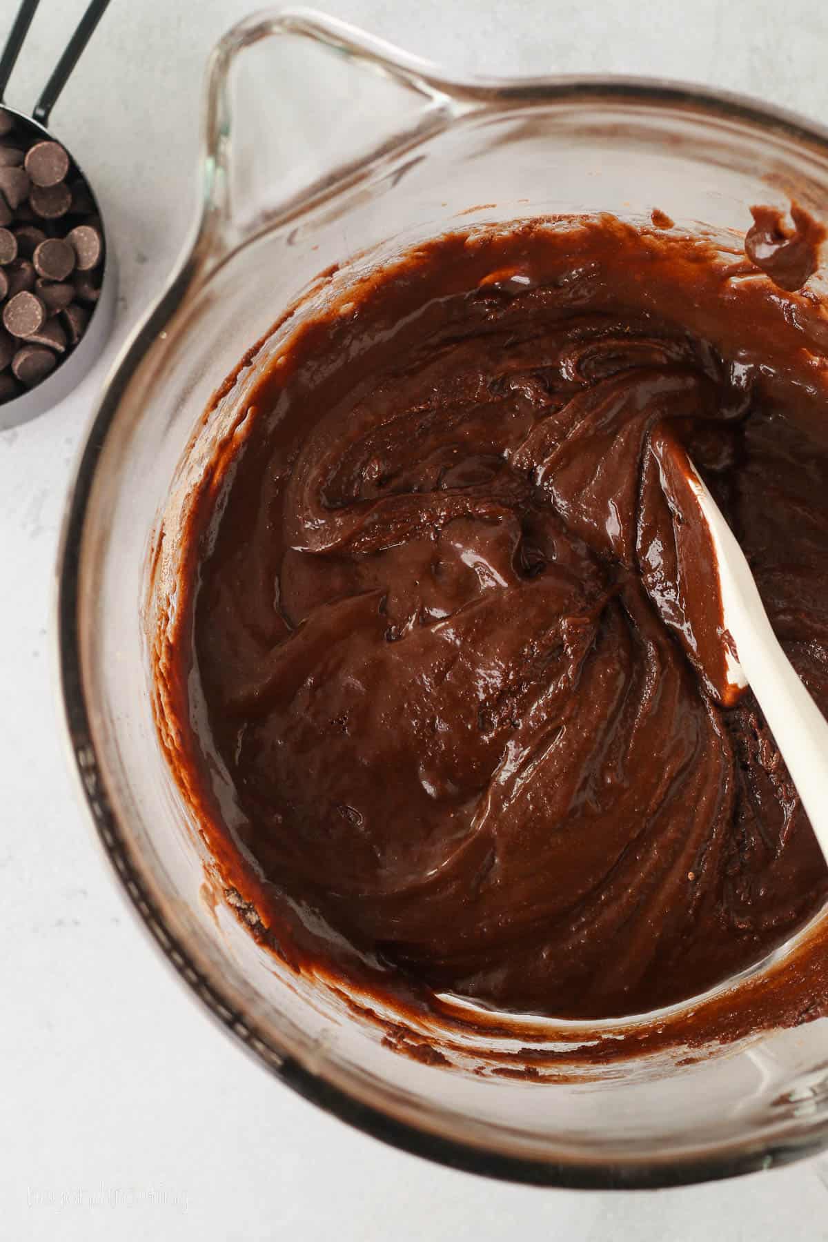 Chocolate brownie batter in a large glass bowl with a spoon.