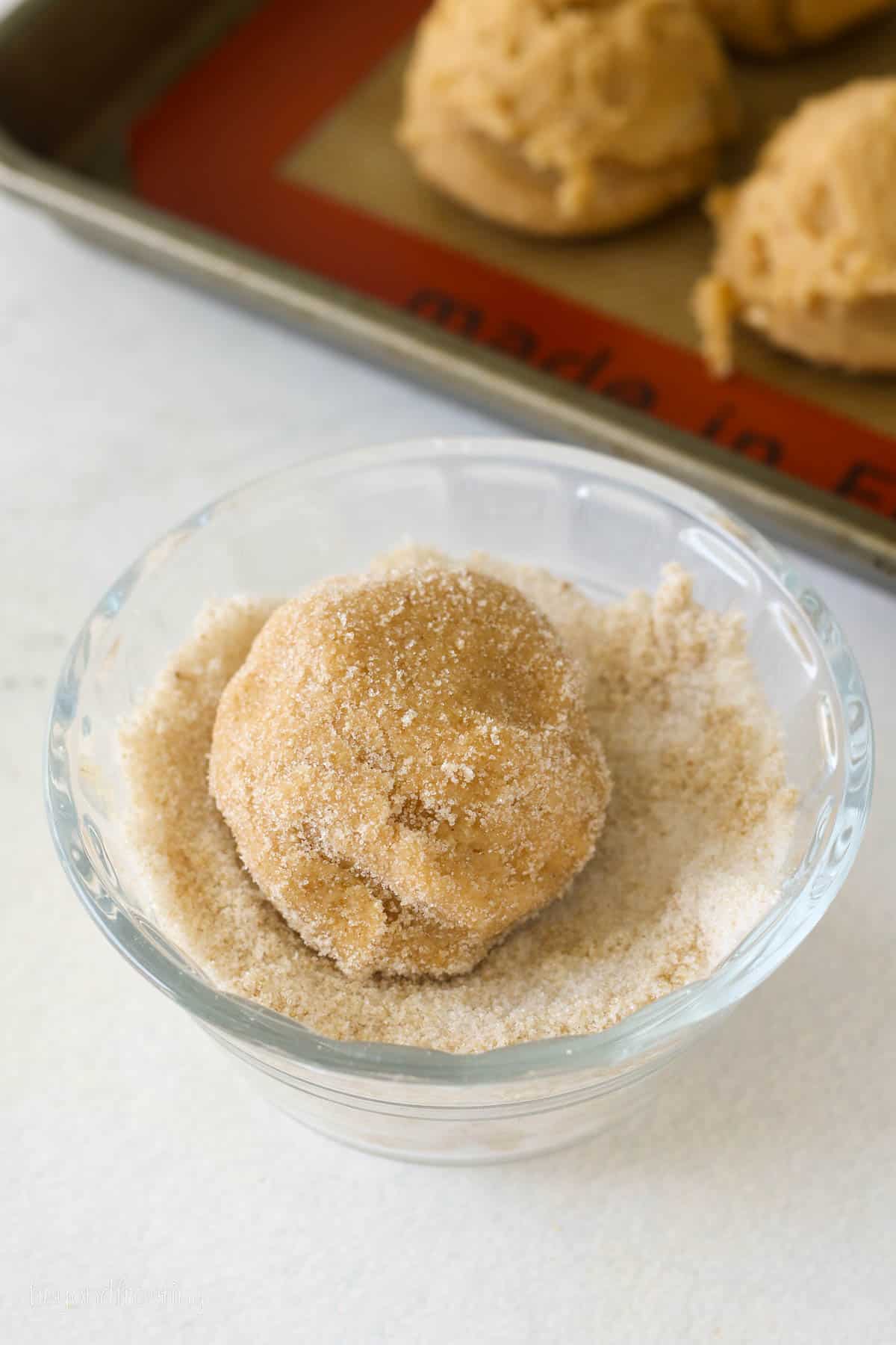 A ball of pumpkin sugar cookie dough rolled in a small bowl of sugar.
