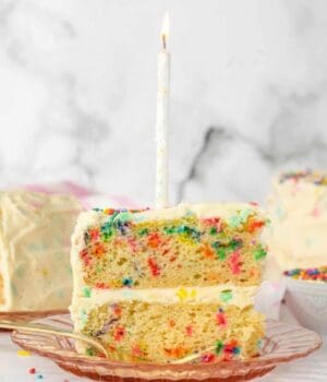 A slice of frosted confetti cake topped with a birthday candle.