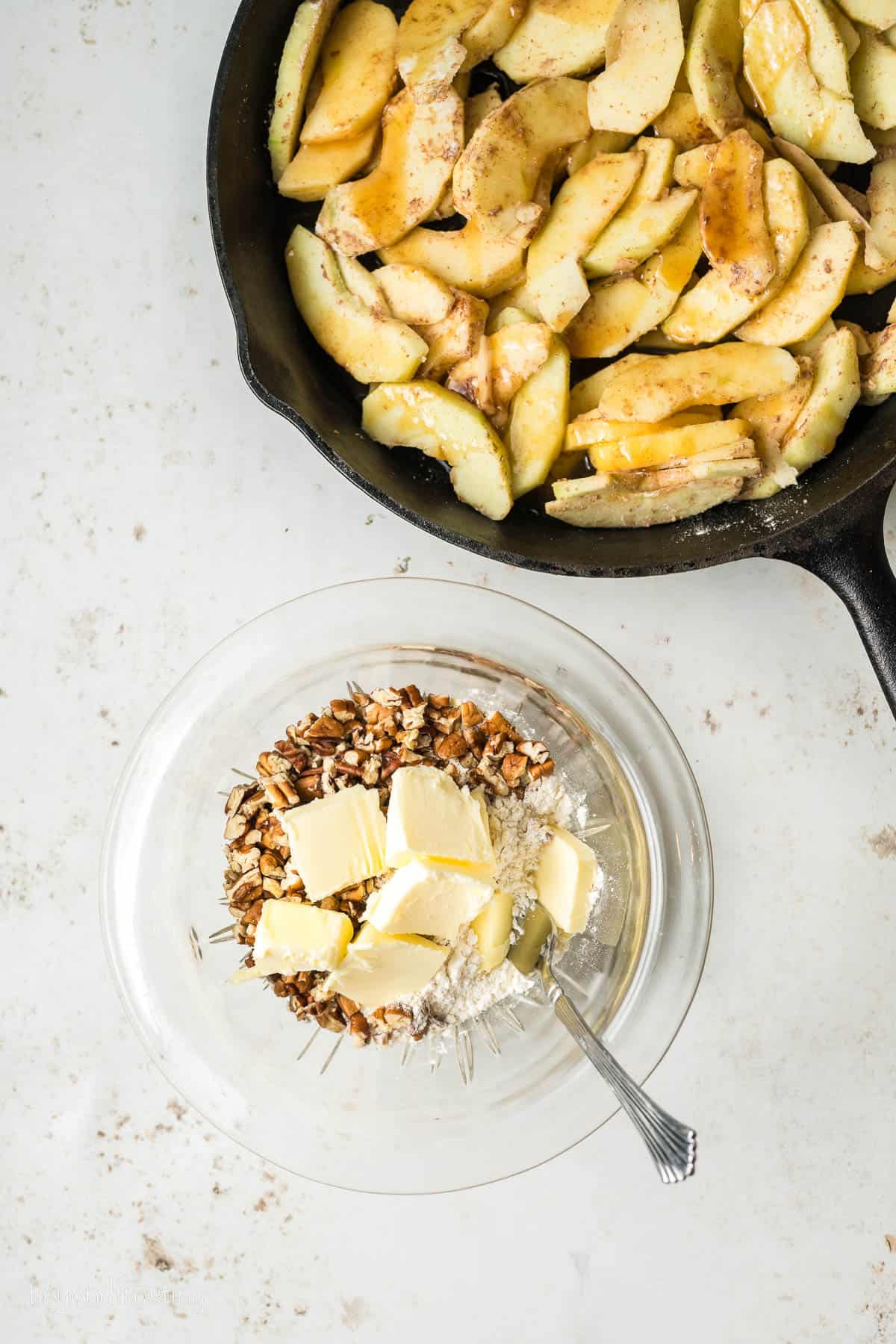 Sauted apples in a skillet next to a bowl of oats combined with cubed butter for the struesel.