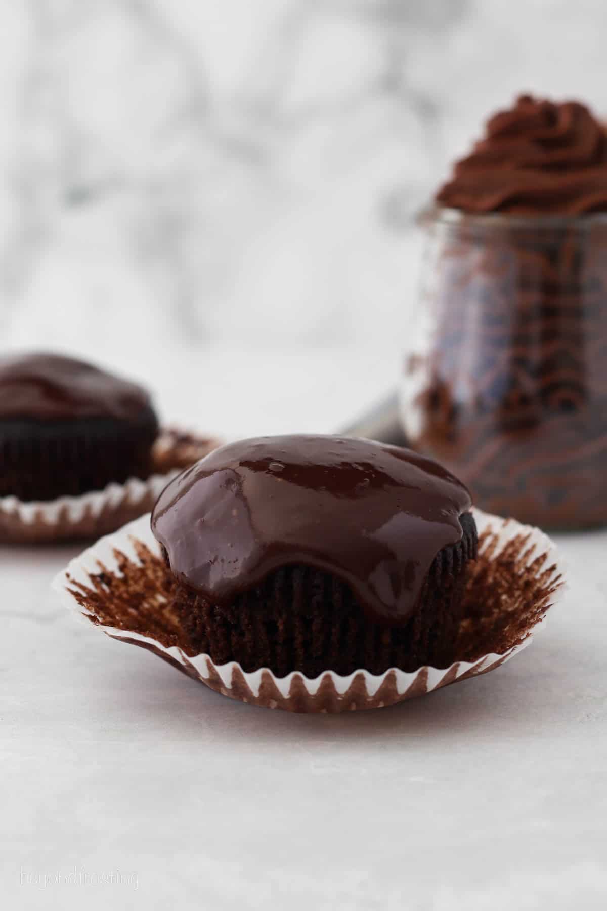 An unwrapped chocolate cupcake covered with chocolate ganache on a countertop.