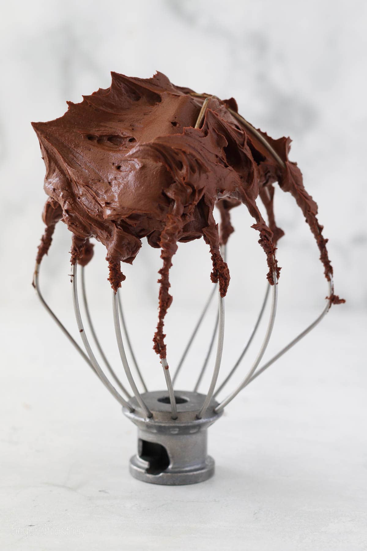 A stand mixer attachment topped with whipped ganache frosting.