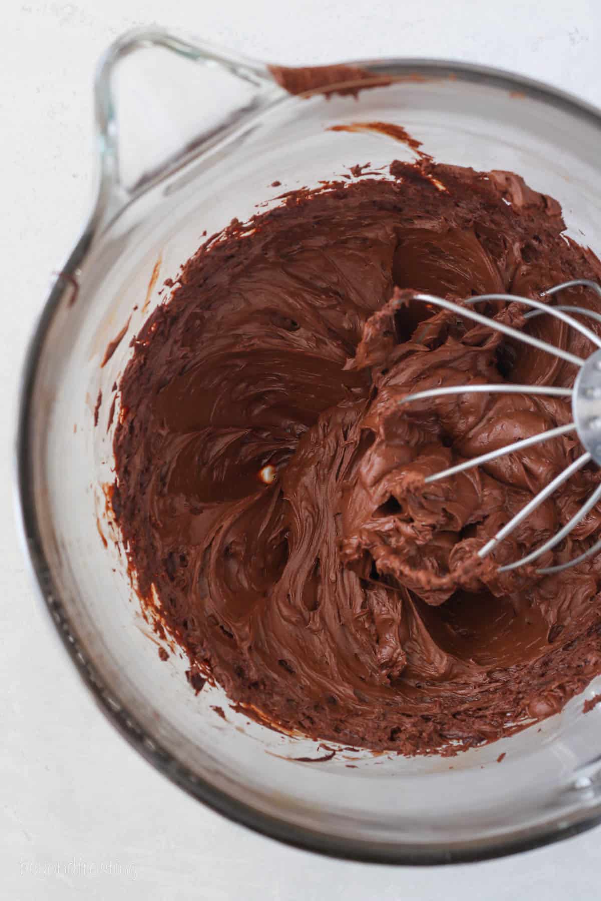 Overhead view of whipped ganache frosting in a bowl with a stand mixer attachment.