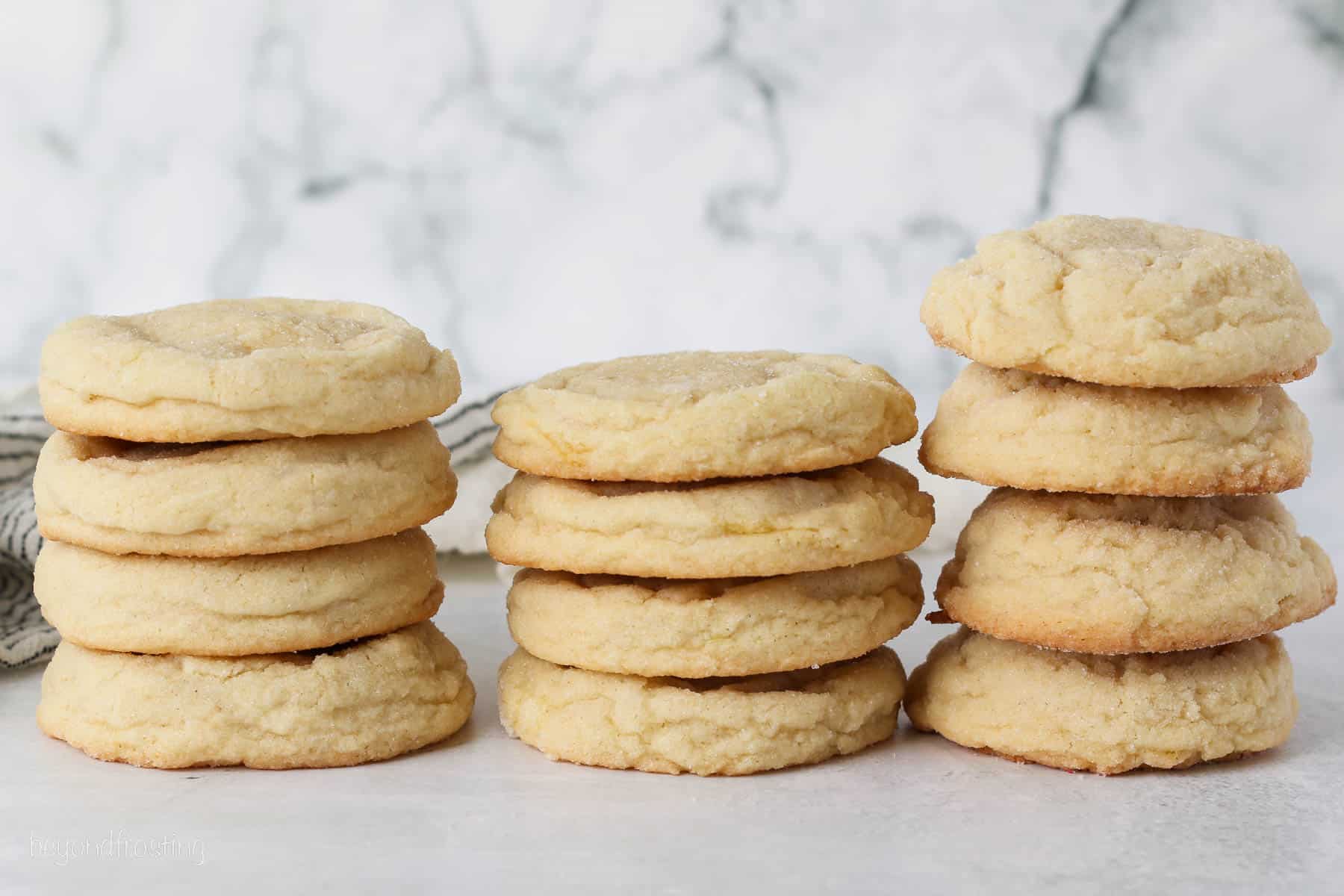 Side view of three stacks of sugar cookies, showing the differences when baked with cream of tartar, lemon juice, or baking powder.